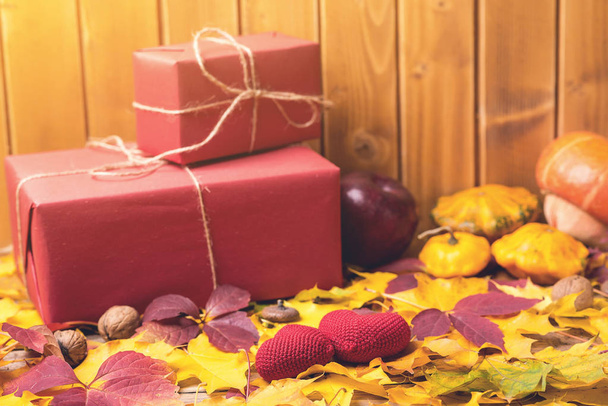 Fond d'automne avec boîtes cadeaux, feuilles d'érable, citrouilles, pommes, coeurs tricotés sur des planches en bois. Concept vacances d'automne et ventes saisonnières
. - Photo, image