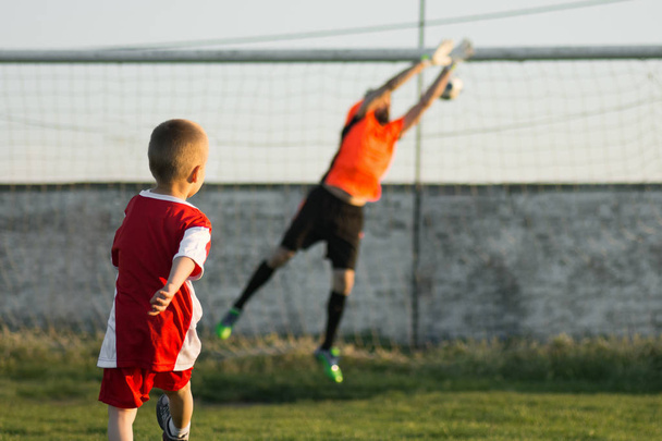 The little 4 years old boy as soccer player is kicking a goal to goalkeeper outdoors on playing field. Soccer sport training for children concept. - Photo, Image