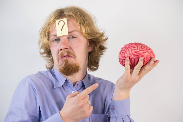 Νεαρός που παίζει με ανθρώπινο εγκεφαλικό μοντέλο. Ο άνθρωπος ανακαλύπτει την καινοτομία και σκέφτεται έχοντας ερωτηματικό στο κεφάλι του. - Φωτογραφία, εικόνα