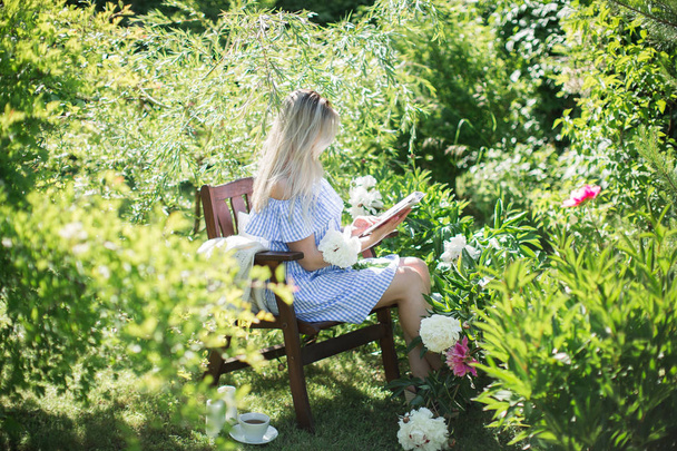 young woman is resting in the garden on a chair with a mug of tea - Fotoğraf, Görsel