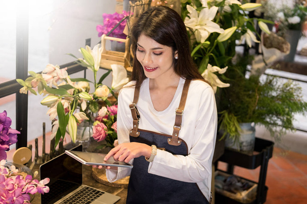 Флорист, стоящий у ее цветочного магазина и использующий ее телефон, чтобы принять заказы на ее магазин, работает небольшой бизнес в городе
. - Фото, изображение