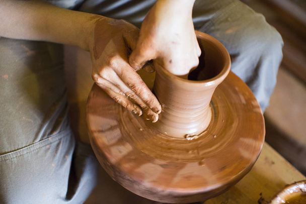 Auf der Vase rotierende Töpferscheibe und Tonwaren: von oben aufgenommen. Hände in Ton. Keramik: männlicher Keramiker stellt ein handgemachtes Produkt aus Ton her. Prozess der Drehung der Töpferscheibe, der Hände des Keramikers. - Foto, Bild
