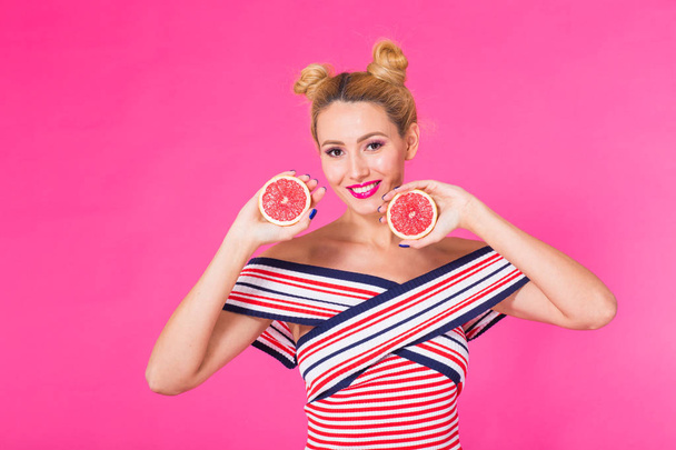 Buena comida para un estilo de vida saludable. Hermosa mujer joven sosteniendo pieza de naranja sobre fondo rosa
 - Foto, Imagen