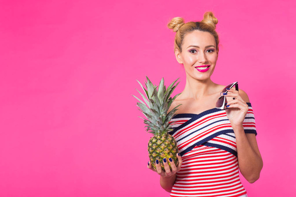 Happy young woman holding a pineapple on a pink background with copyspace. - Foto, immagini