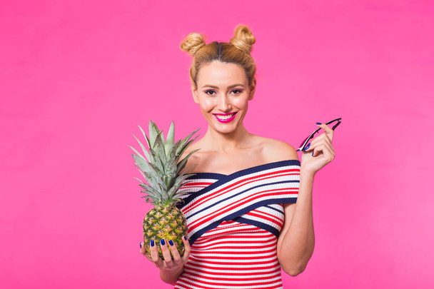 glückliche junge Frau mit einer Ananas auf rosa Hintergrund. Sommer-, Ernährungs- und Urlaubskonzept - Foto, Bild