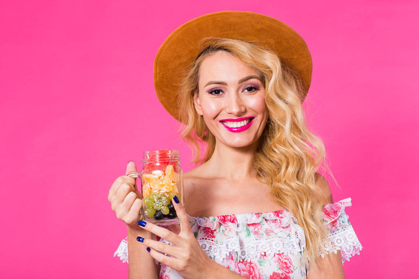 Young beautiful woman with fruit jar on pink background - Фото, изображение