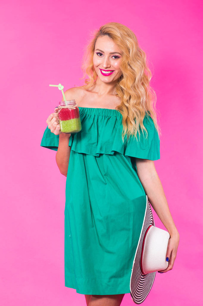 Mooie jongedame met groene smoothie op roze achtergrond - Foto, afbeelding