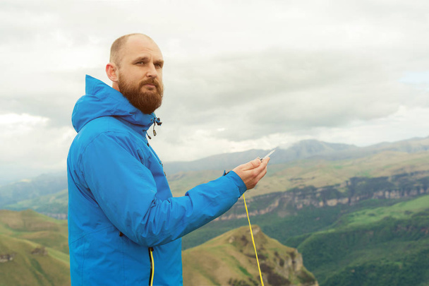 Hipster man in a blue jacket using a compass on the background in the background of the Caucasian landscape with a plateau - Photo, image