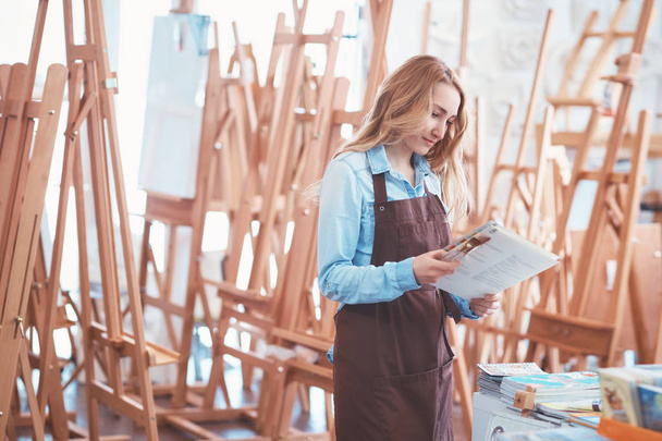 Young artist in an apron on the background of easels - Photo, Image