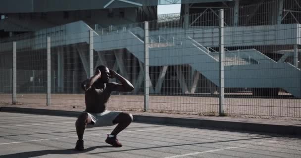 Sporty African American man doing squats outdoors near the sports stadium. Workout, fitness, health, beauty, motivation concept. Shot in Red Epic - Filmati, video