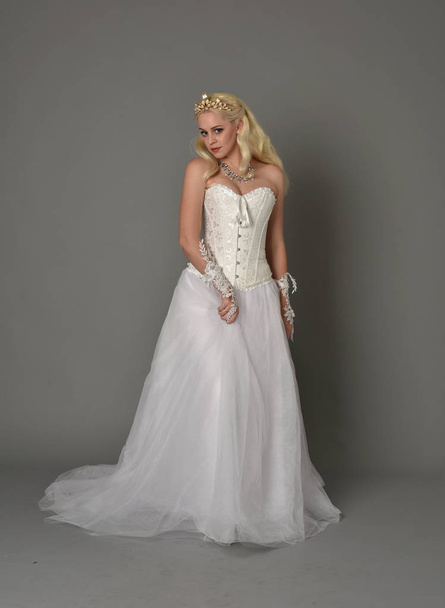 full length portrait of blonde girl wearing white corset gown. standing pose on grey studio background. - Photo, Image