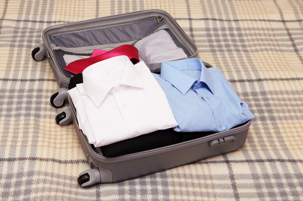 Open grey suitcase with clothing on plaid - Foto, immagini