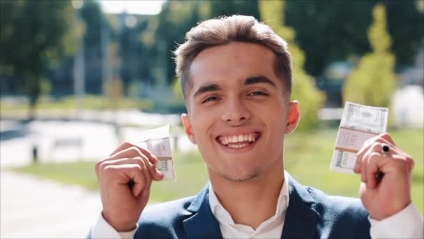 Happy young businessman holding a big amount of money in his hands. He stands in the street near the office center or bank. Business style, winnings, deposit, success, career - Filmati, video