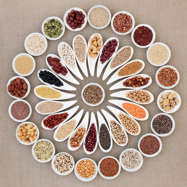 Vegan high protein dried health food collection with nuts, seeds, legumes, pasta, grains and cereals. Foods high in fiber, antioxidants, anthocyanins, vitamins and minerals. Top view on hessian background. - Фото, изображение