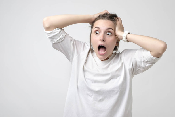 Portrait of surprised beautiful caucasian girl holding her head in amazement and open-mouthed. Concept of great shock on sale or news - Photo, Image