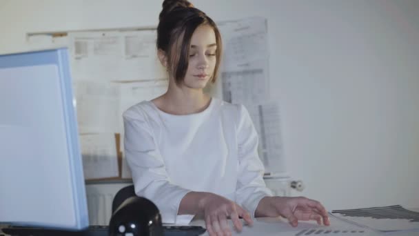 Pretty young girl is busy at workplace and smiles at camera. - Séquence, vidéo