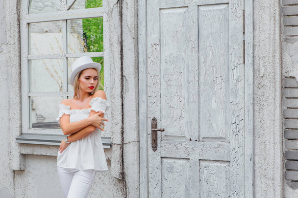 Sexy modern bride in white cylinder hat lstanding next to old white vintage door and mirror window. Copy space. - Valokuva, kuva
