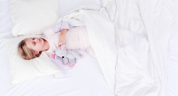 Child little girl sleeps in the bed with a toy teddy bear - Zdjęcie, obraz