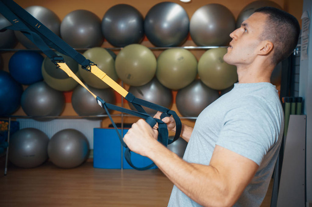 νεαρός άνδρας δραστηριοποιείται σε ένα γυμναστήριο για το trx - Φωτογραφία, εικόνα