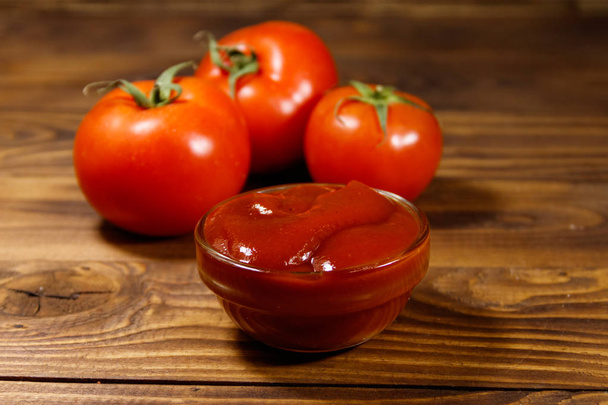 Скляна миска кетчупу або томатного соусу і свіжі стиглі помідори на дерев'яному столі
 - Фото, зображення
