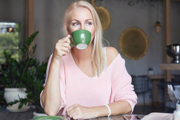 Cropped shot of good looking cheerful American female holds cup of coffee, has lunch in cozy cafeteria, rests after excursion, recreates in resort country, expresses positive emotions and feelings. - Foto, Bild