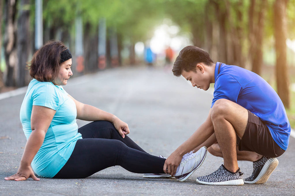 Injury from workout concept : The asian man use hands hold on his ankle of fat woman while running on road in the park. Focus on ankle. - Φωτογραφία, εικόνα
