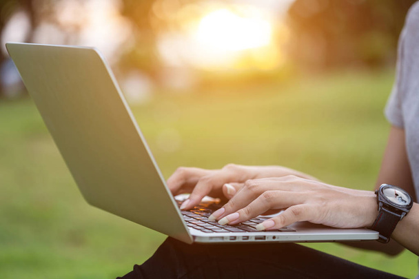 Крупним планом жінка сидить в парку під час заходу сонця і використовує ноутбук
 - Фото, зображення
