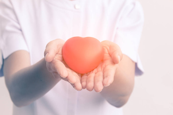 Senior female nurse holding red heart symbol in her 2 hands; isolate on white - Photo, Image