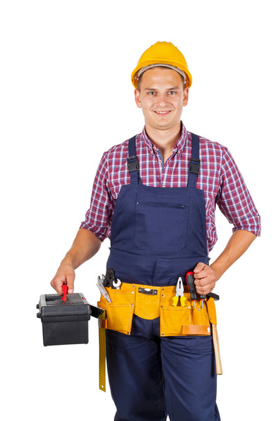 Attractive young repairman with yellow helmet and tool belt on isolated background - Foto, Bild