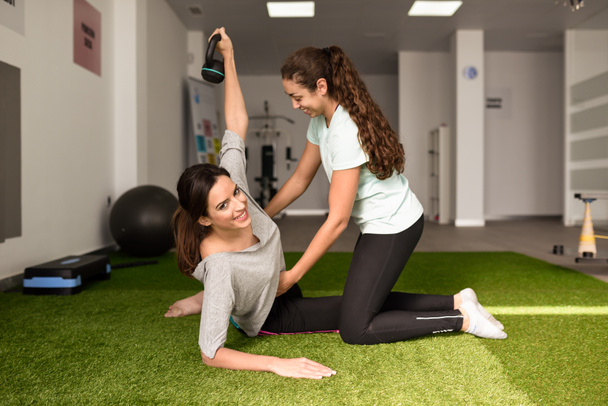 Physiothérapeute aidant jeune femme caucasienne avec l'exercice avec haltère pendant la réadaptation dans la salle de gym à l'hôpital. Physiothérapeute féminine formant un patient dans un centre de physiothérapie
. - Photo, image