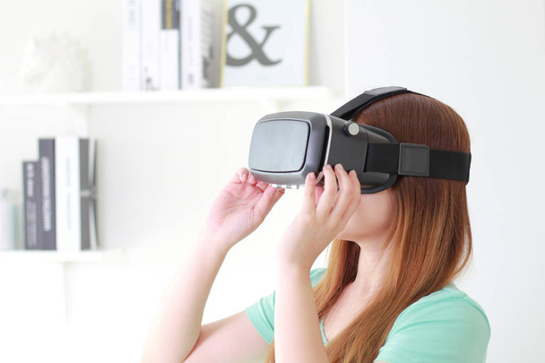 Jovem mulher usando óculos de realidade virtual em casa. Um fone de ouvido de realidade virtual é um dispositivo montado na cabeça que fornece realidade virtual para o usuário
. - Foto, Imagem