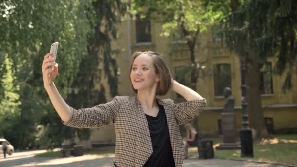 Young attractive girl is making selfie in park in daytime, in summer, communication concept - Filmagem, Vídeo