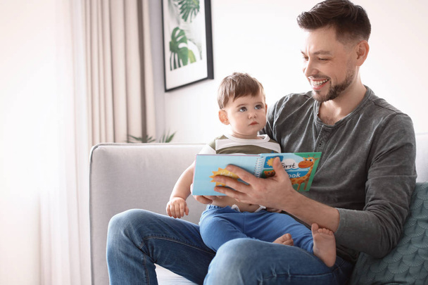 Dad and his son reading book on sofa at home - Photo, Image