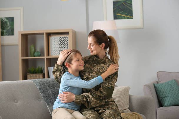 Woman in military uniform with her little son on sofa at home - 写真・画像