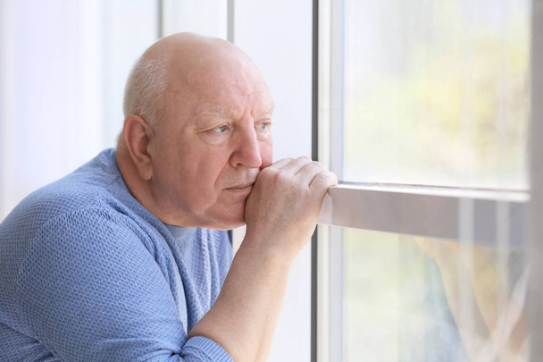 Depressed senior man near window indoors - Fotó, kép