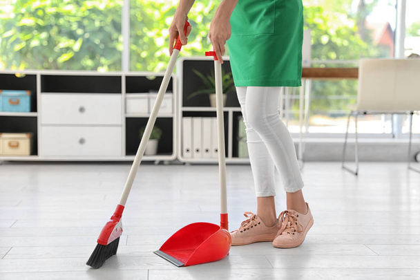Young woman with broom and dustpan cleaning in office - Foto, Imagem