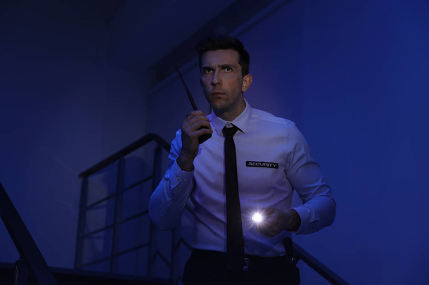 Male security guard with flashlight and portable radio transmitter in dark room - Φωτογραφία, εικόνα