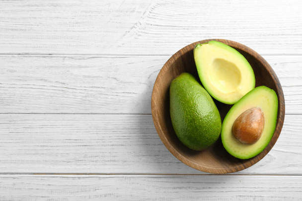 Bowl with ripe avocados on wooden background, top view - Valokuva, kuva