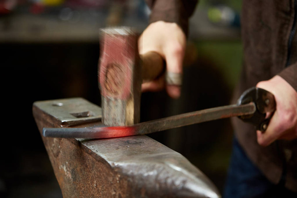 Close-up of a blacksmiths hands manipulating a metal piece above his forge, selective focus. - Foto, immagini