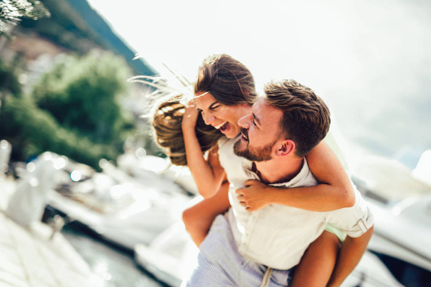Casal de turistas desfrutando de férias de verão à beira-mar, mulher alegre piggybacking jovem namorado
 - Foto, Imagem