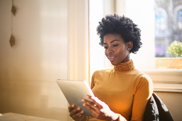 Young beautiful Afro woman smiling and surfing on the internet on a tablet. - Foto, Bild