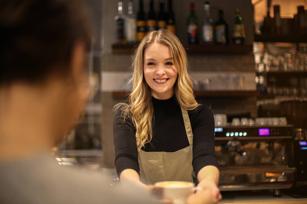 Joven hermosa camarera rubia sirviendo a un cliente en un bar y sonriendo
. - Foto, imagen