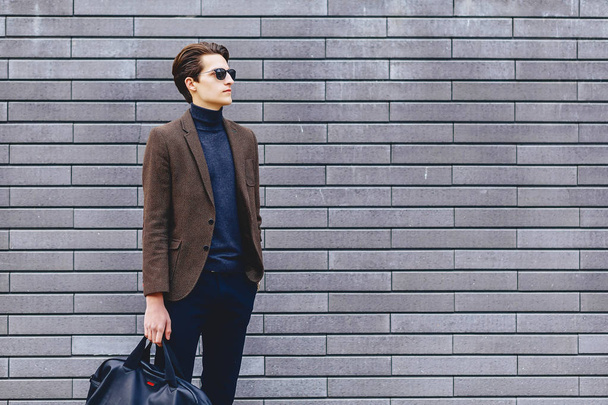 stylish guy in jacket and sunglasses against the background of wall - Fotó, kép