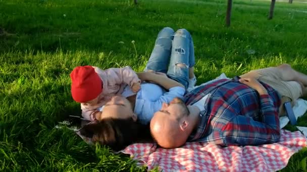 Happy family lies and rests on the nature, a small child takes a smartphone in his hands - Imágenes, Vídeo