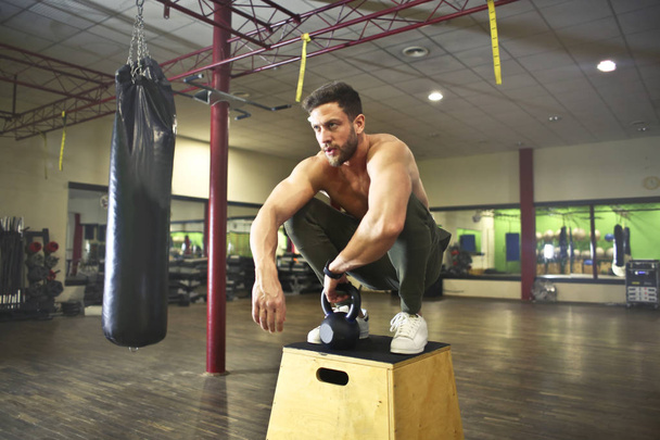Young handsome athletic man squat on a gym furniture. - Foto, afbeelding