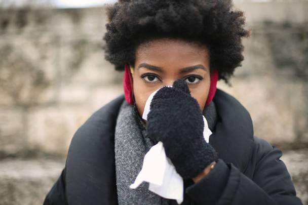 Young Afro woman in winter blowing her nose. - Фото, зображення