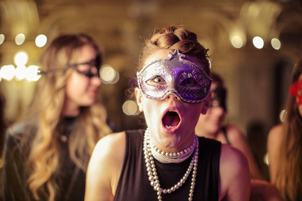 Νεαρή γυναίκα σε μια μάσκα σε μια φορεσιά κόμμα με μια φοβισμένη έκφραση. - Φωτογραφία, εικόνα