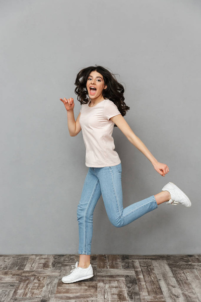Image of beautiful young lady jumping isolated over grey background wall looking camera. - 写真・画像