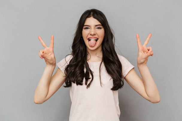 Photo of pretty cute young lady standing isolated over grey background wall showing peace gesture. - Foto, Imagem