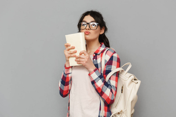 Image of pretty cute young lady student standing isolated over grey background wall holding book. - 写真・画像